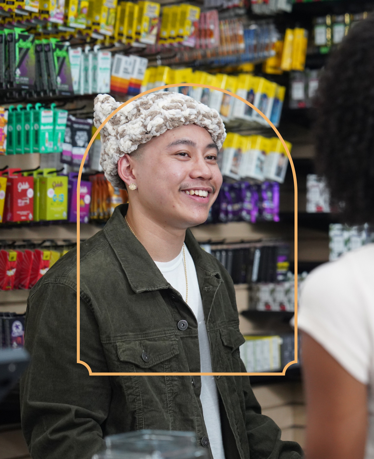 Cannabis retailer in a knit hat talks to a dispensary customer blurred in the foreground